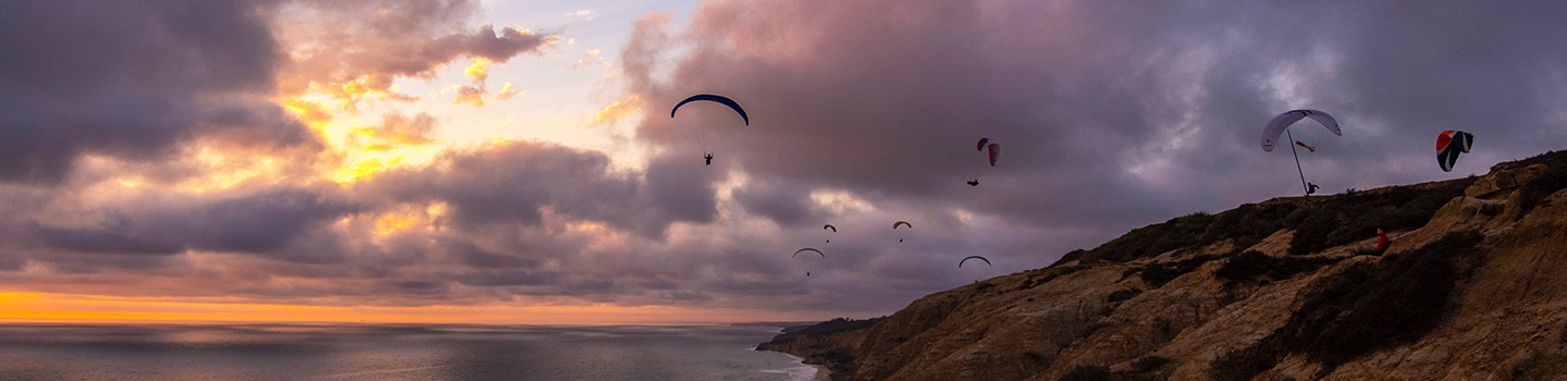 Hangliders float against a cloudy evening sky, above the bluffs at La Jolla near UC San Diego campus
