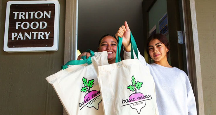 Two smiling students hold up canvas Food Pantry bags on campus at UCSD's Basic Needs Hub