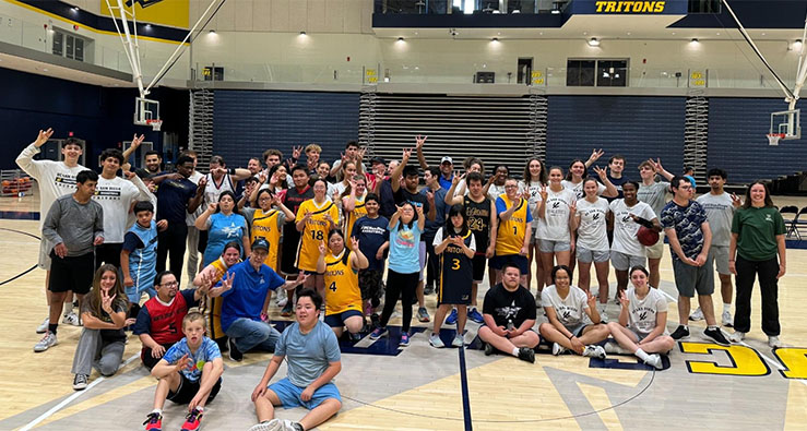 Large group of UCSD Triton men's and women's basketball teams pose with Special Olympics athletes on the basketball court at RIMAC