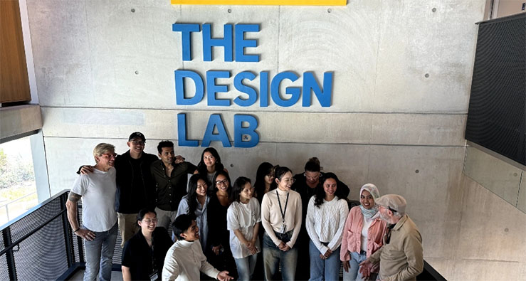Group of smiling UCSD students and staff on the stairs at the Design Lab