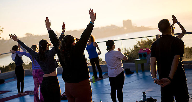 Silhouettes of people reaching their arms to the sky in a sunset yoga class, La Jolla, UCSD