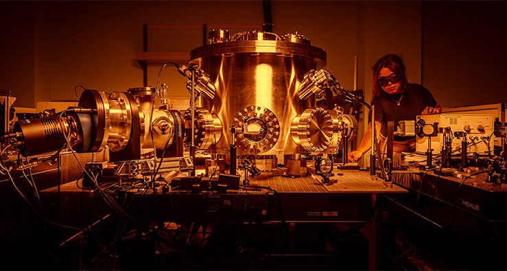 A researcher with heavy goggles looks over a large generator