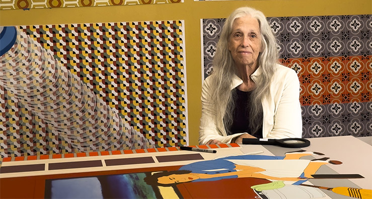 Marge Dean sits at a table surrounded by art and design posters