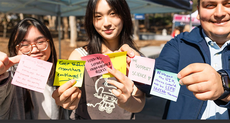 UCSD students hold up stickie notes, supporting federal research funding