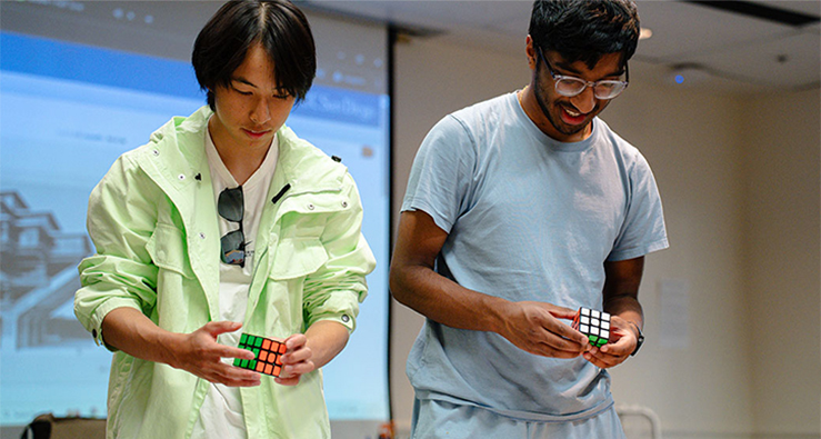 Two UCSD students stand next to one another, looking down at their hands that are manipulating a Rubik's Cube