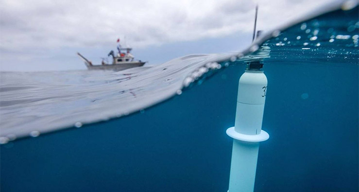 Argo program data collection device bobs in the ocean with a Scripps research vessel in the background