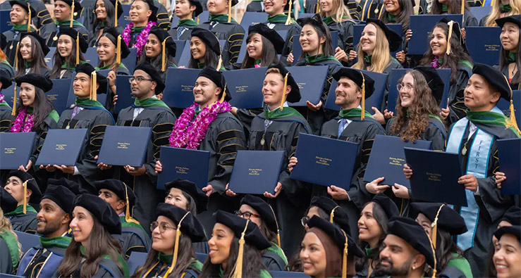 Large group of smiling UCSD School of Medicine graduates in their black caps and gowns, holding up their diplomas