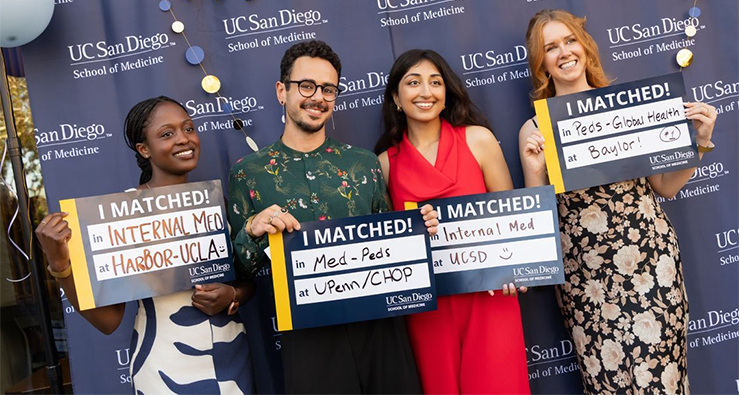 Four smiling UC San Diego School of Medicine students show off placards showing where they are headed for their residencies
