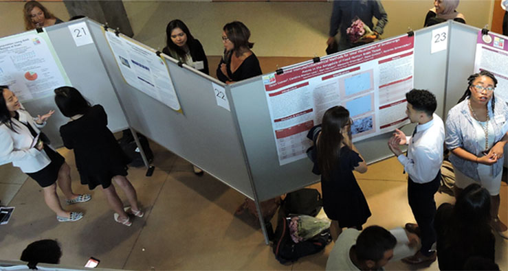 UC San Diego students mingle and chat in front of rows of research posters - Undergrad Research Conference, May 20, 2024